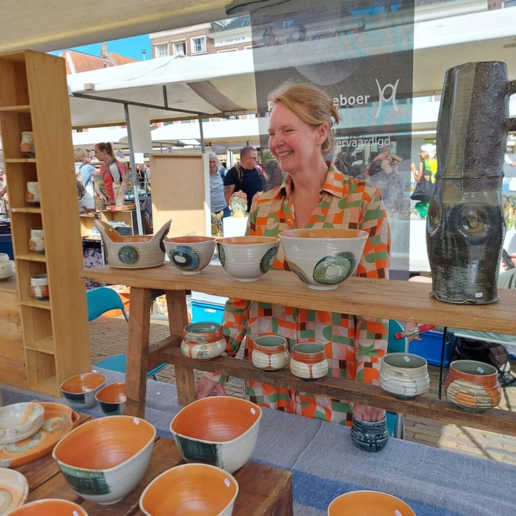 Pauline Hoeboer staat lachend achter haar kraam op de keramiekmarkt in Swalmen